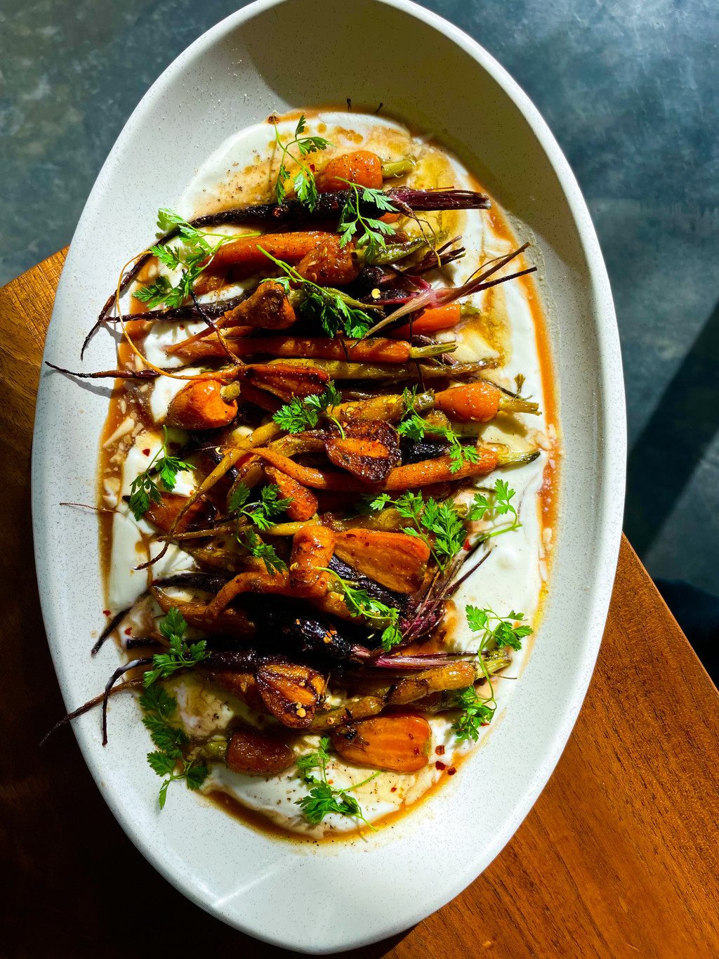 A white dish with bright roasted carrots and chicken with ricotta and green parsley