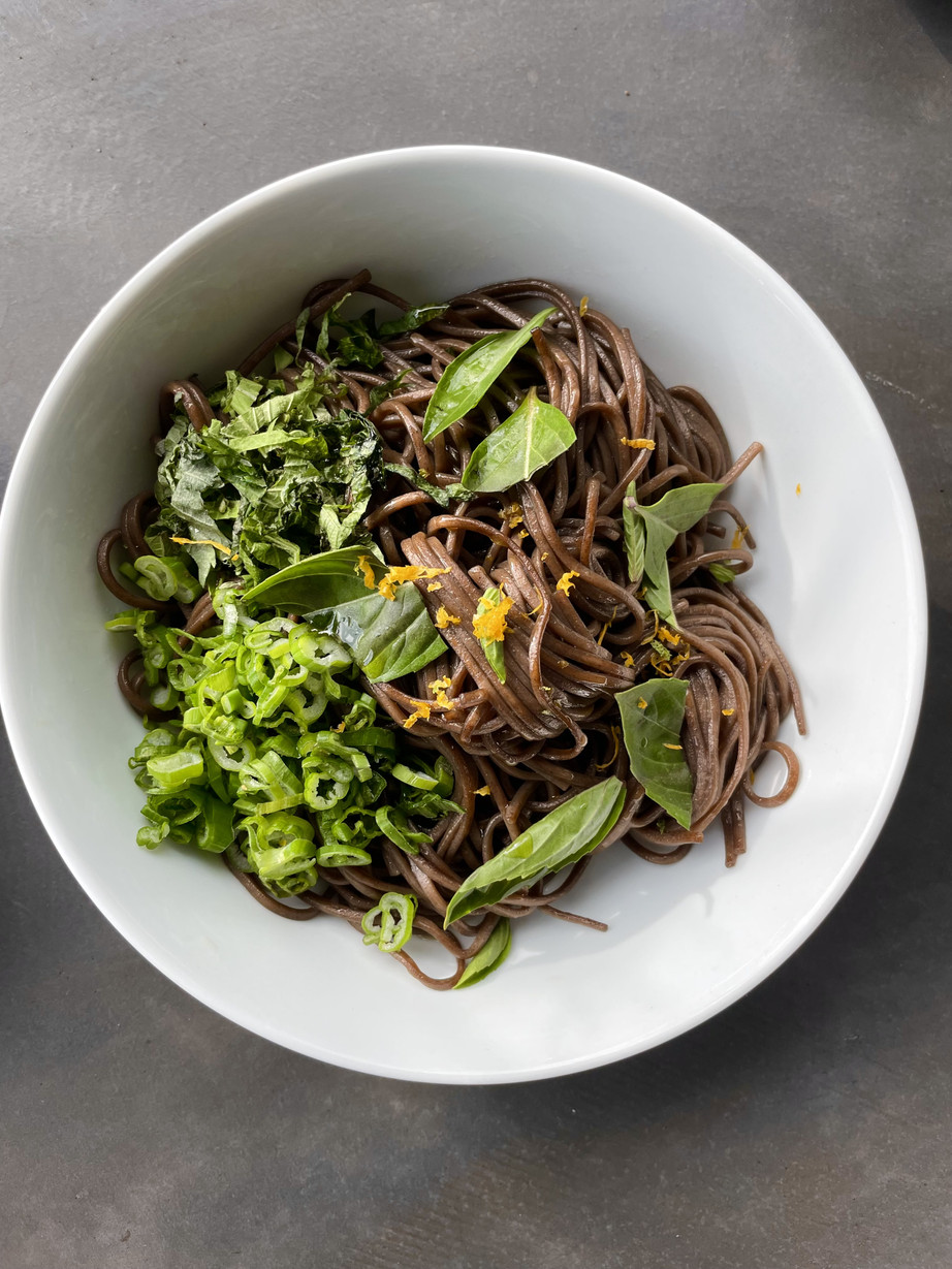 A dish of twisted soba noodles with fresh herbs on top